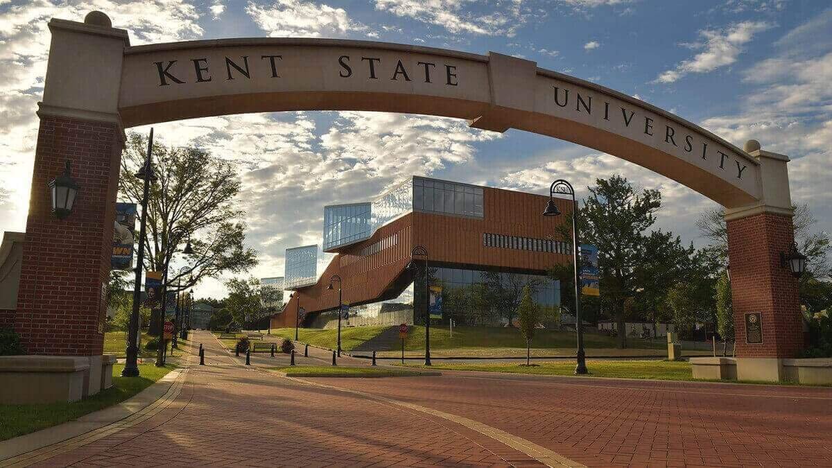 Entrance archway to Kent State University with a modern academic building in the background, captured on a sunny day with a partly cloudy sky. The Scoop Ninjas provide pooper scooper services in Kent OH