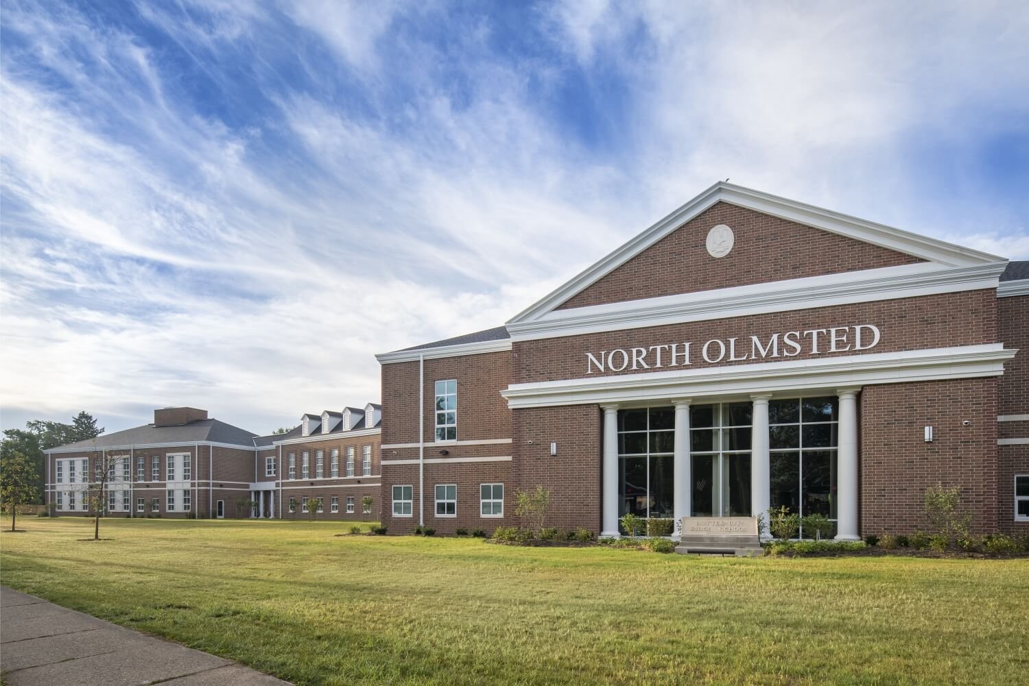 Exterior view of a large brick building labeled "North Olmsted" under a blue sky with light clouds, surrounded by a well-maintained grassy lawn.