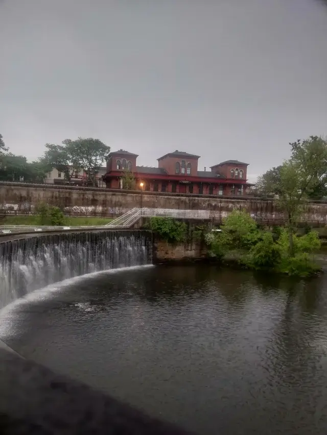 Scenic view of a curved waterfall along the Cuyahoga River in Kent, Ohio, with the historic red Kent train depot building in the background on an overcast day. The Scoop Ninjas provide pooper scooper services in Kent OH
