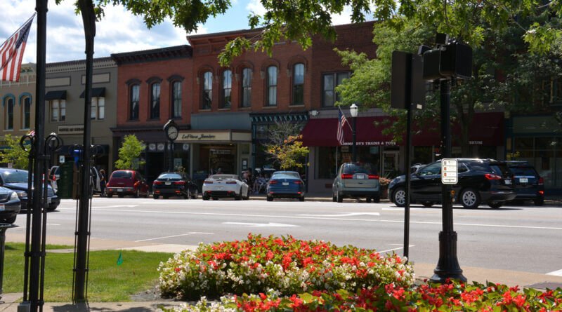 Downtown Medina, Ohio featuring historic brick storefronts, American flags, parked cars, and colorful flower beds along the main street.
