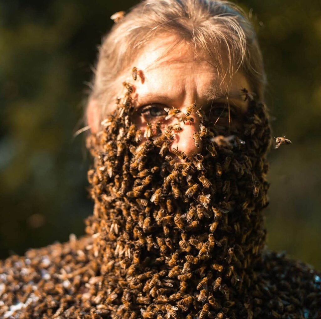 Beekeeper covered in live bees at Mueller Honey Bee Co., showcasing pollinator importance in partnership with The Scoop Ninjas for eco-friendly pet waste solutions.