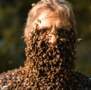 Beekeeper covered in live bees at Mueller Honey Bee Co., showcasing pollinator importance in partnership with The Scoop Ninjas for eco-friendly pet waste solutions.